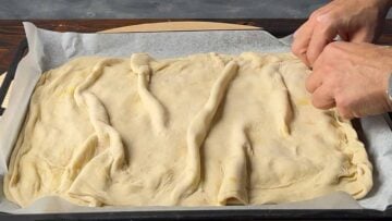 Two hands seal the edges of the Tiropita.