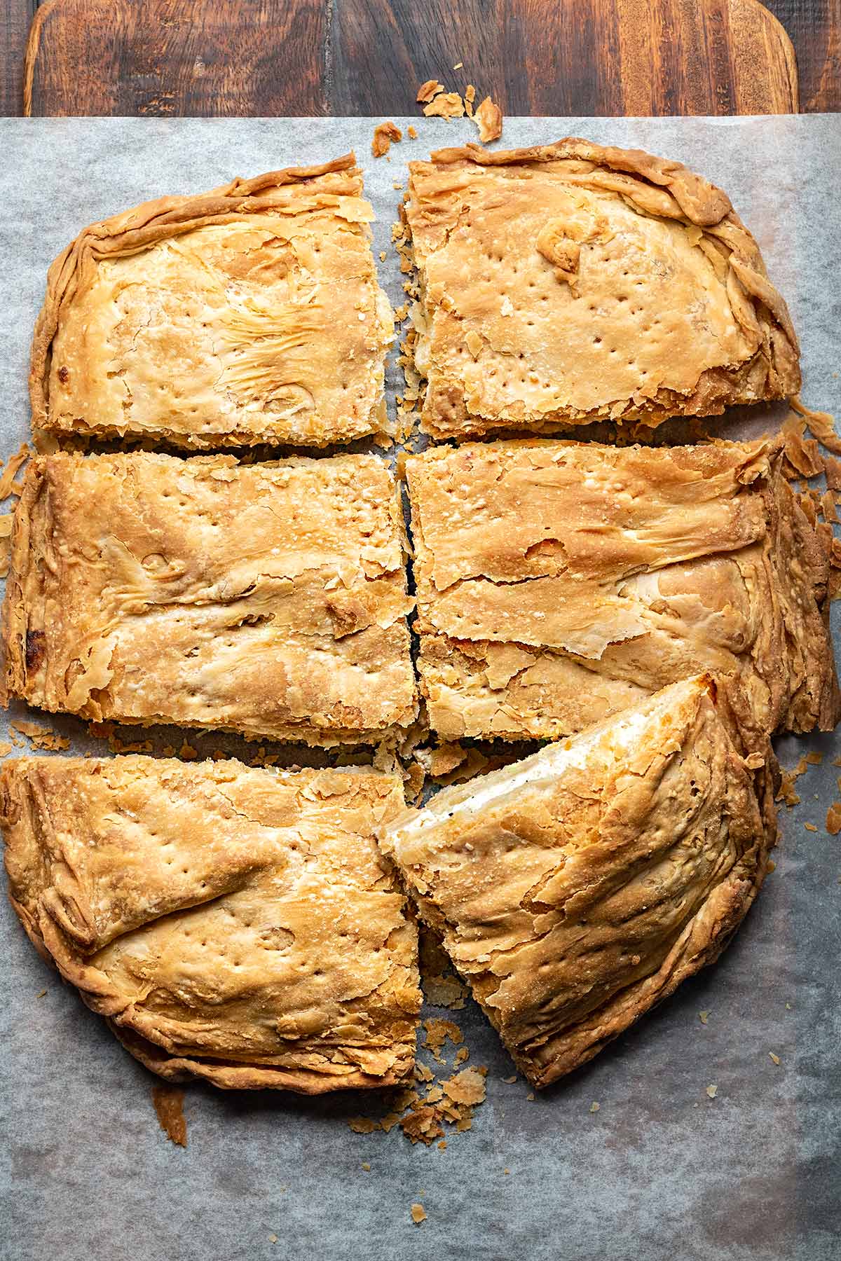 Greek cheese pie cut in pieces on a piece of parchment paper.