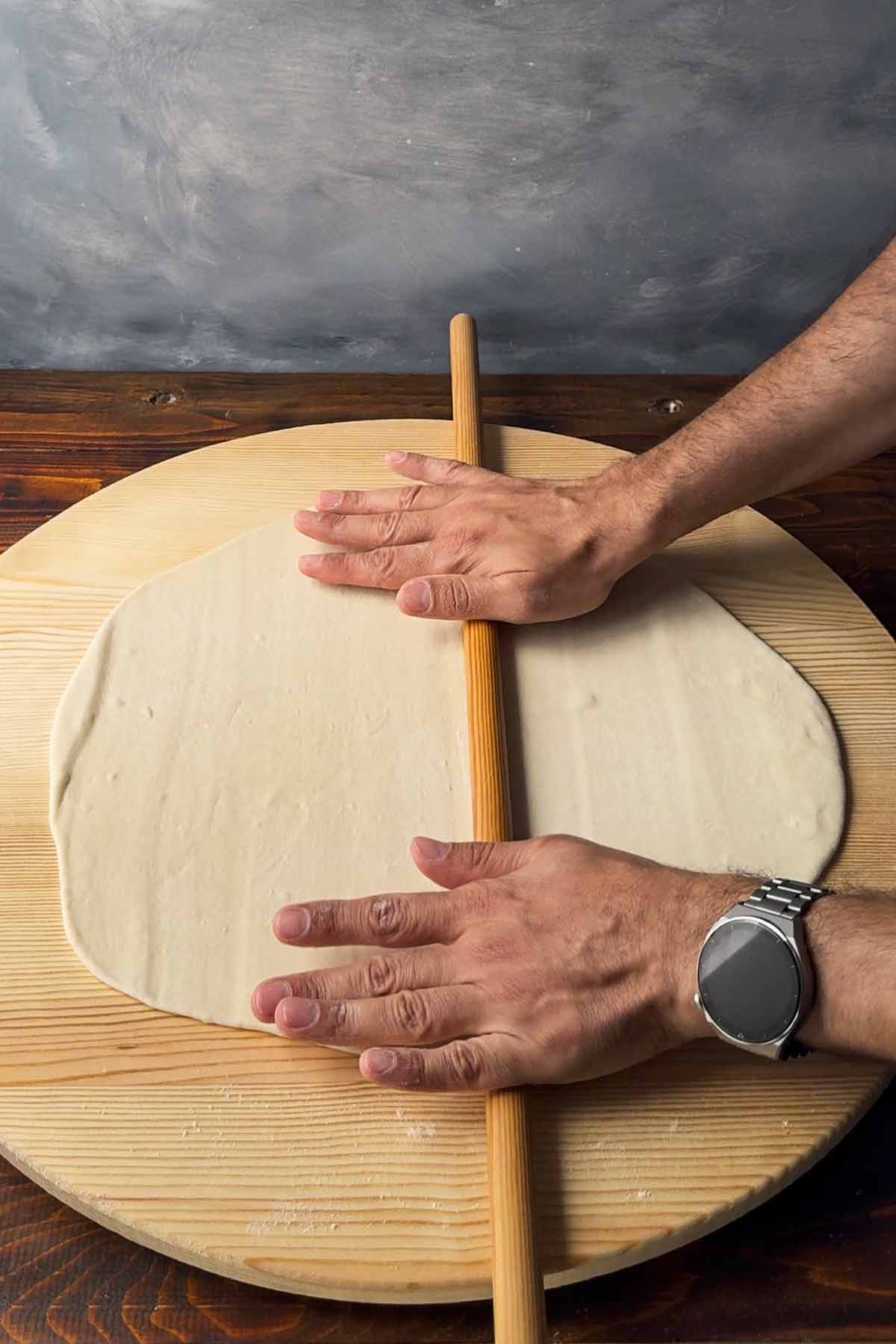 Two hands rolling phyllo dough with a rolling pin.