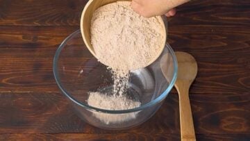 A hand adding flour to a mixing bowl.