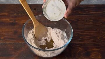 A hand adding Greek yogurt to a bowl with flour.