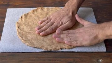 Two hands shaping pizza dough into a disc.